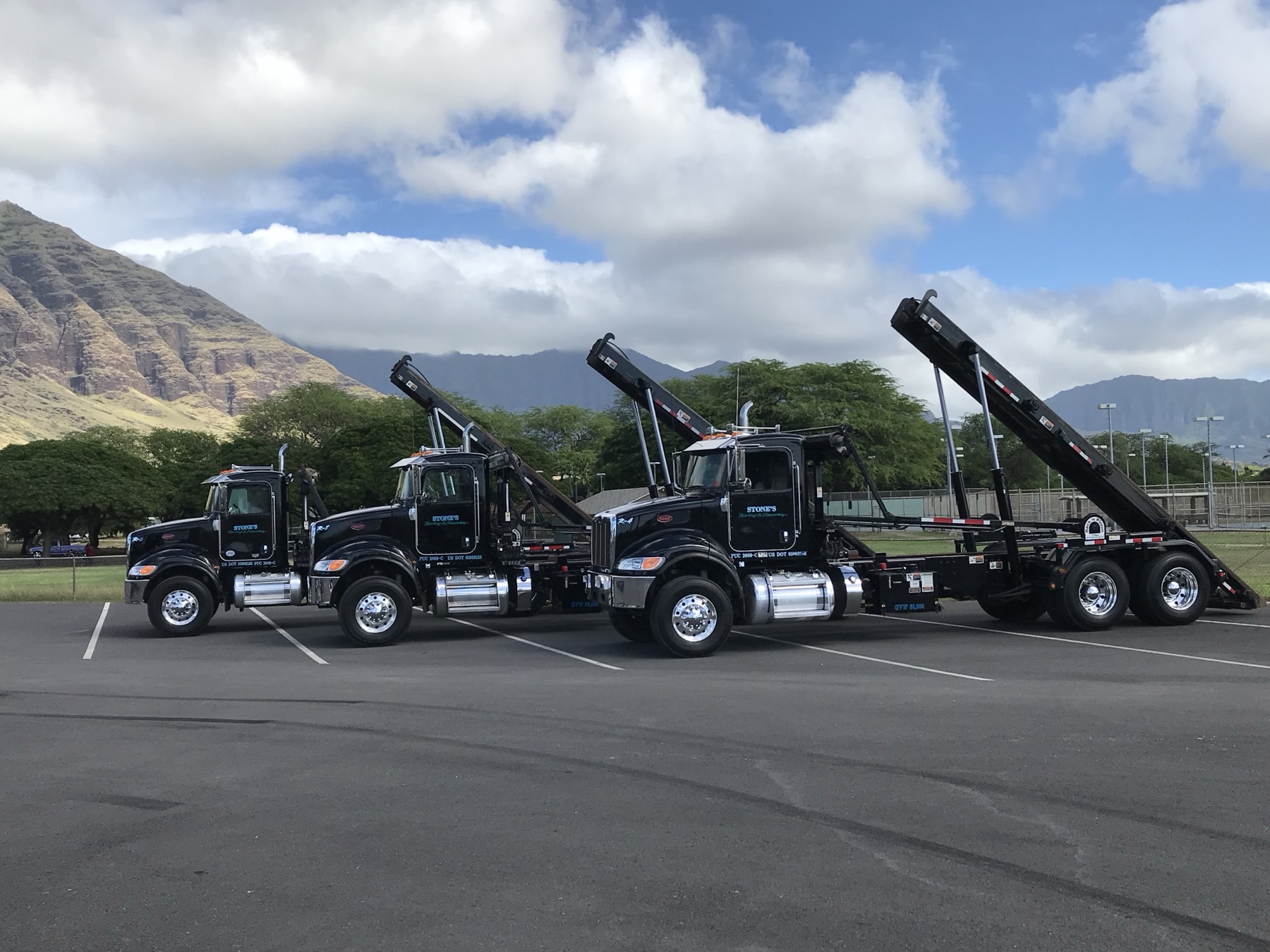 Stone's Towing & Recovery roll-off fleet parked with the Waianae mountains behind them, Oahu