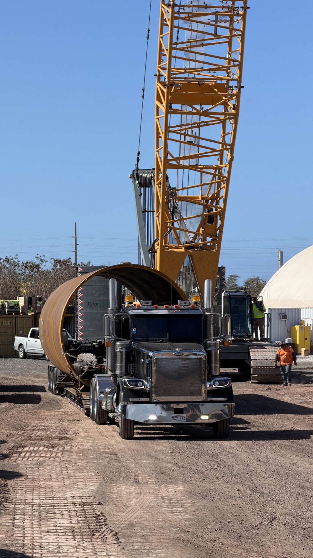 Stone's truck hauling large industrial pipe under crane support
